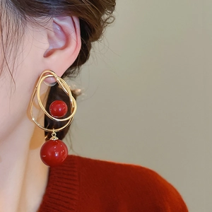 Détail de boucles d'oreilles doubles boucles dorées avec perles rouge foncé sur un mannequin