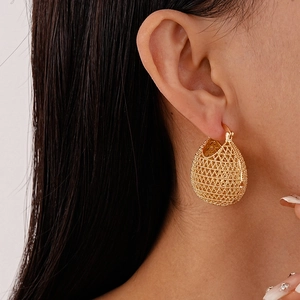 Close-up of a gold mesh teardrop earring with intricate woven texture on a female model