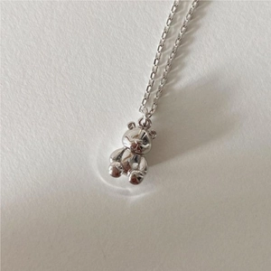 Macro shot of a 3D silver bear pendant necklace on a warm white textured surface