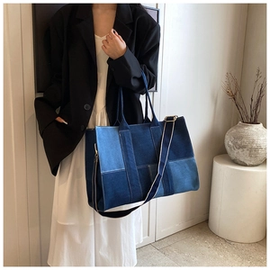 Model wearing a large denim patchwork tote bag with an adjustable crossbody strap