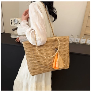 Detail of a khaki woven straw tote bag featuring orange and beige tassels with wooden beads