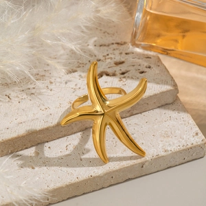 Golden starfish ring on beige stone with white feather and perfume bottle