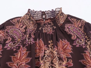Detail of bohemian paisley print high neck with smocked frill trim on brown chiffon dress