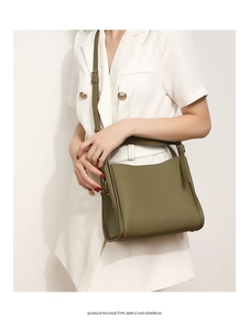 Detail shot of green pebbled leather bucket bag on a white suit model in a minimalist setting
