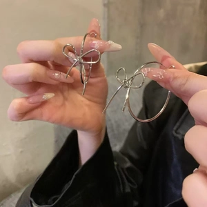 Silver bow hoop earrings held by hand, minimalist metal jewelry for women