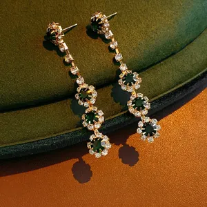 Luxury floral emerald crystal drop earrings with gold tassels on velvet background