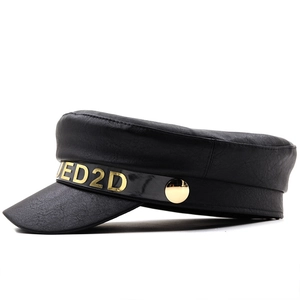 Dettaglio del cappello baker boy in ecopelle nera con lettere in metallo dorato