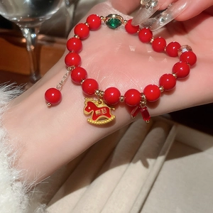 Detail of red beaded bracelet with golden rocking horse charm and emerald gemstone