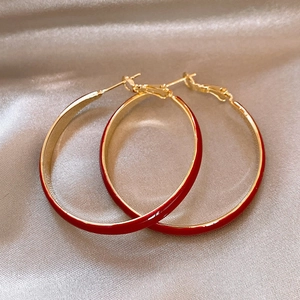Detailed close-up of red enamel hoop earrings on champagne silk fabric background