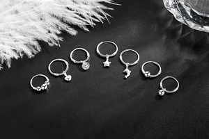 Detailed macro view of 7-piece S999 silver earring set with assorted charms on black background