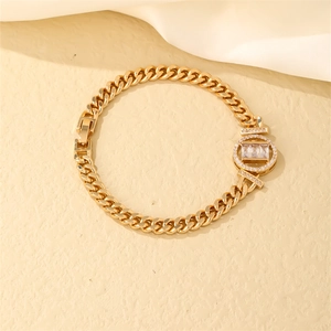 Detail of gold curb chain bracelet with baguette-cut zircon center and fold-over clasp