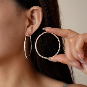Polished silver geometric hoop earrings with textured finish shown on model