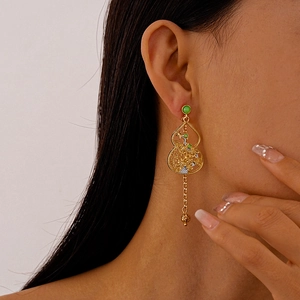 Close-up of golden hollow gourd earrings with green beads on a model's ear