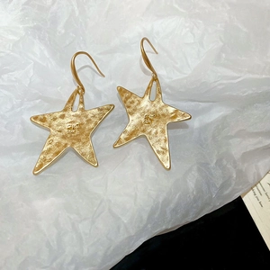 Macro shot of gold star-shaped hammered metal earrings on white textured background
