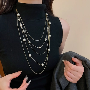 Detail of layered gold chain necklace with various white pearls on a black top