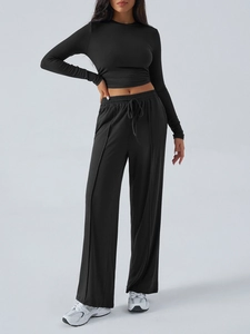 Studio shot of black yoga set featuring long sleeve crop top and wide-leg drawstring pants