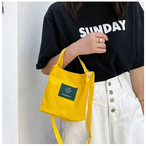 Close-up of a mini yellow canvas bucket bag with a green patch label on a street style model