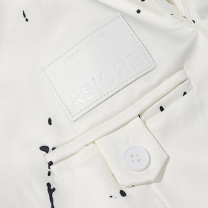 Detail of white blazer showing twill fabric texture, ink splash pattern and leather logo tag