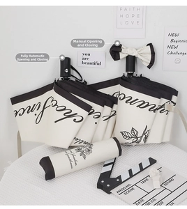 Detail of automatic and manual cream folding umbrellas with black trim and floral pouch