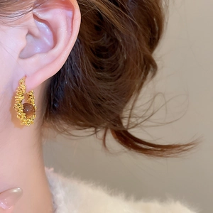 Close-up of golden hoop earrings with brown resin beads worn on ear with soft fur collar