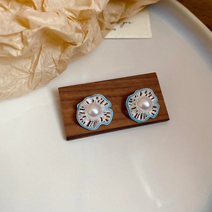 Detail of blue enamel flower stud earrings with white pearl center on wooden display