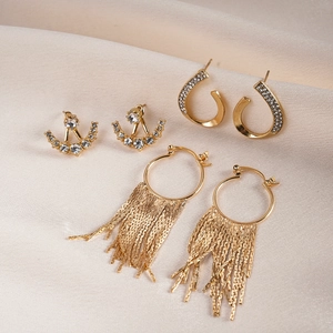 Detailed view of three gold rhinestone earrings with geometric fringe and hoops on silk fabric