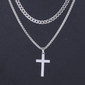 Detail of silver double-layer necklace featuring Cuban links and a simple cross pendant