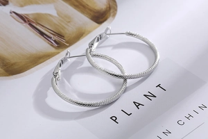 Detail of silver hoop earrings with spiral rope texture on a white magazine background