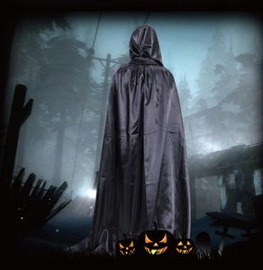 Rear view of a long black hooded Halloween cape made of smooth satin in a spooky forest