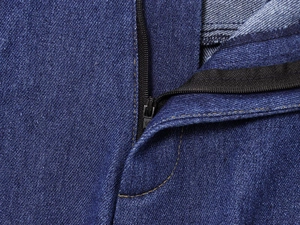 Dettaglio macro della cerniera e delle cuciture gialle a contrasto sui jeans blu scuro