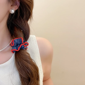 Close-up of denim ruffle scrunchie with red trim detailing on a low ponytail