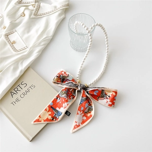 Detail of French vintage pearl necklace with red printed silk bow on white background