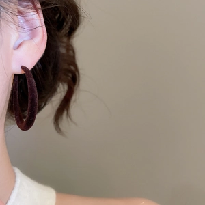 Détail de créoles en forme de C floquées marron foncé sur un modèle avec texture douce
