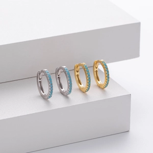 Detailed shot of silver and gold huggie earrings with turquoise blue stones on cubes