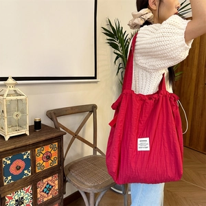 Side view of large rose red drawstring tote bag carried by a model in lifestyle setting