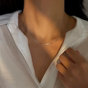 Elegant minimalist gold snake bone chain necklace worn on a white shirt in warm sunlight