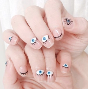Detailed view of evil eye nail stickers with blue eyes and black lashes on natural nails