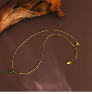 Detail of 18K gold-plated necklace with a green zircon pendant on natural wood background