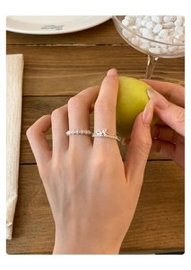 Macro detail of delicate silver bow ring and lace pattern band on a woman's finger