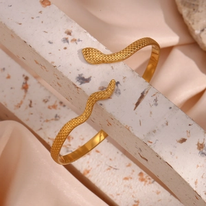 Adjustable snake-shaped gold open bangle with detailed snake scale texture on stone background