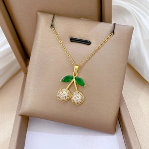 Detail of cherry pendant necklace with green stones and white pavé on beige jewelry stand
