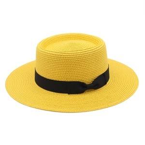 Close-up of a yellow woven flat top straw hat with a black grosgrain ribbon bow
