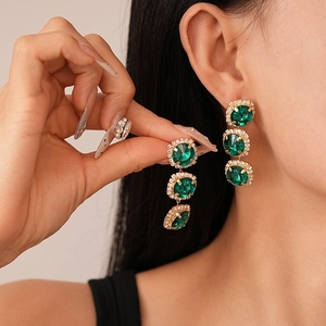 Detail view of gold-plated earrings featuring emerald green stones and sparkling zircon pavé