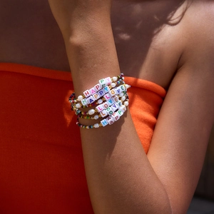 Detail of colorful beaded bracelets with HAPPY and LOVE letter charms on a wrist