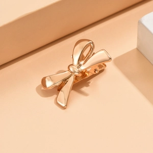 Close-up of a polished golden metal bow hair clip on a minimalist geometric pedestal
