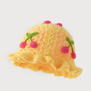 Detailed knit texture of a yellow handmade crochet bucket hat with 3D cherry accents