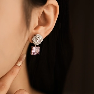 Detail of silver camellia earring with a pink square gemstone on a female model