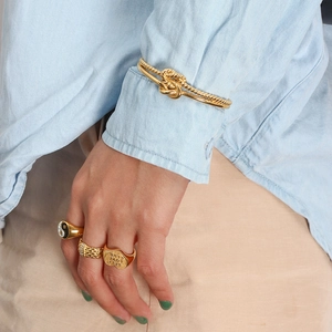 Detail of twisted gold knot bracelet and engraved heart ring on model wrist