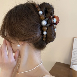 Détail d'une pince à cheveux marron avec perles blanches et perles d'ambre sur chignon