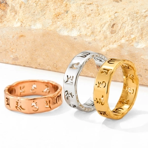 Edelstahlringe mit Sechs-Wort-Mantra in Gold, Silber und Roségold auf Natursteinblock